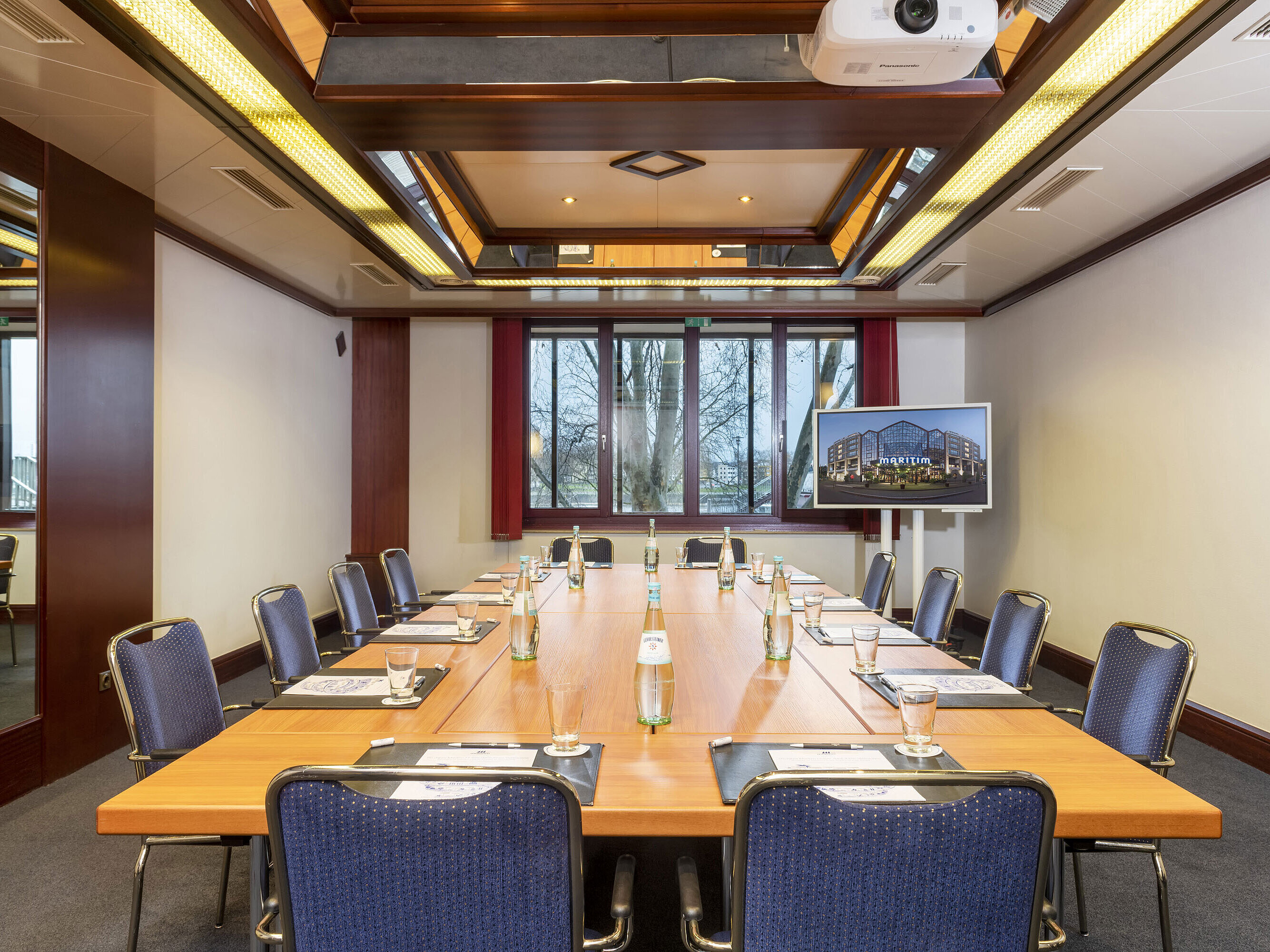 Salon Loreley, a modern conference room with square table setup, projector, and flat screen for presentations.