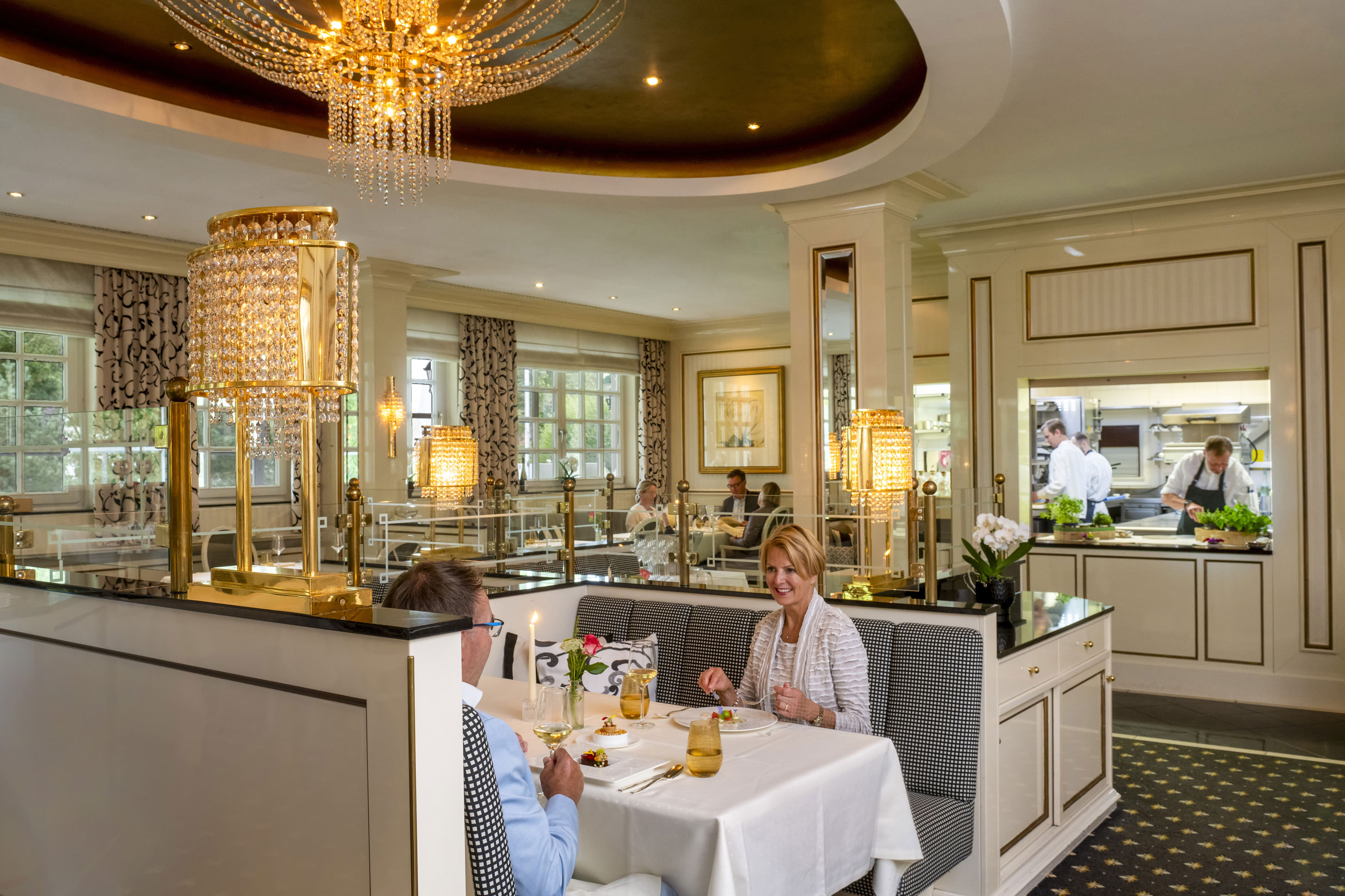 Couple profitant d'un dîner raffiné au restaurant Orangerie du Maritim Seehotel Timmendorfer Strand avec vue sur la cuisine.