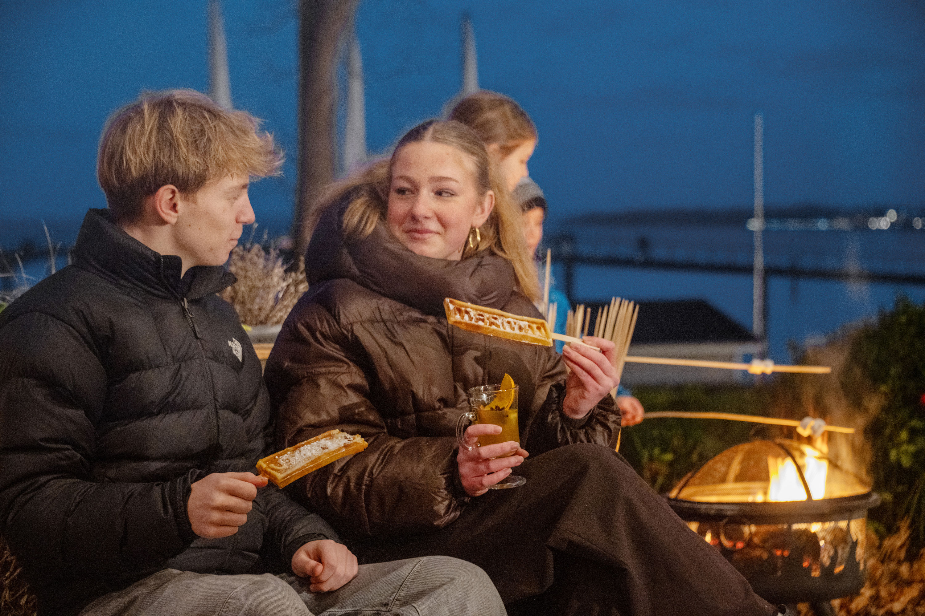 Winter magic by the Baltic Sea Family enjoying freshly baked waffles by a fire basket on a winter-decorated terrace overlooking the Baltic Sea.